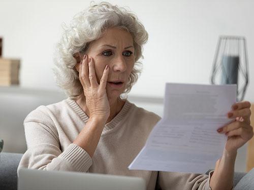 A senior woman looks at a bill with a look of shock